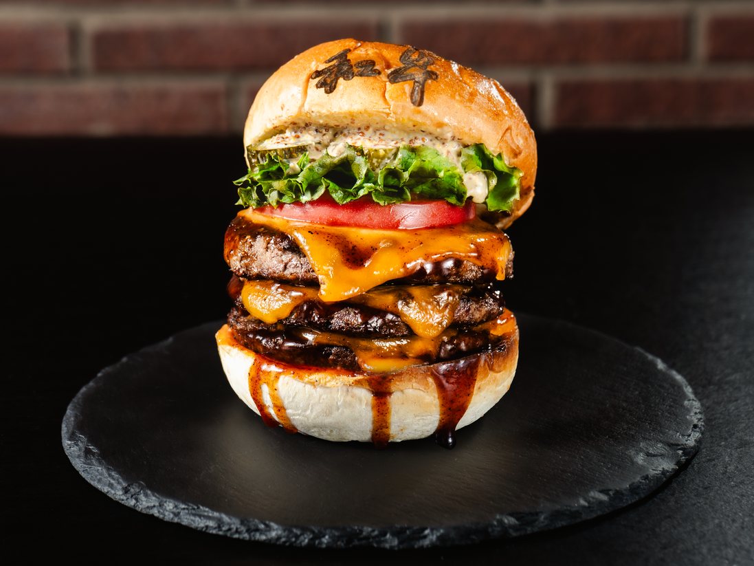 Triple Wagyu cheeseburger with lettuce, tomato and a bun branded 和牛, on a black slate plate